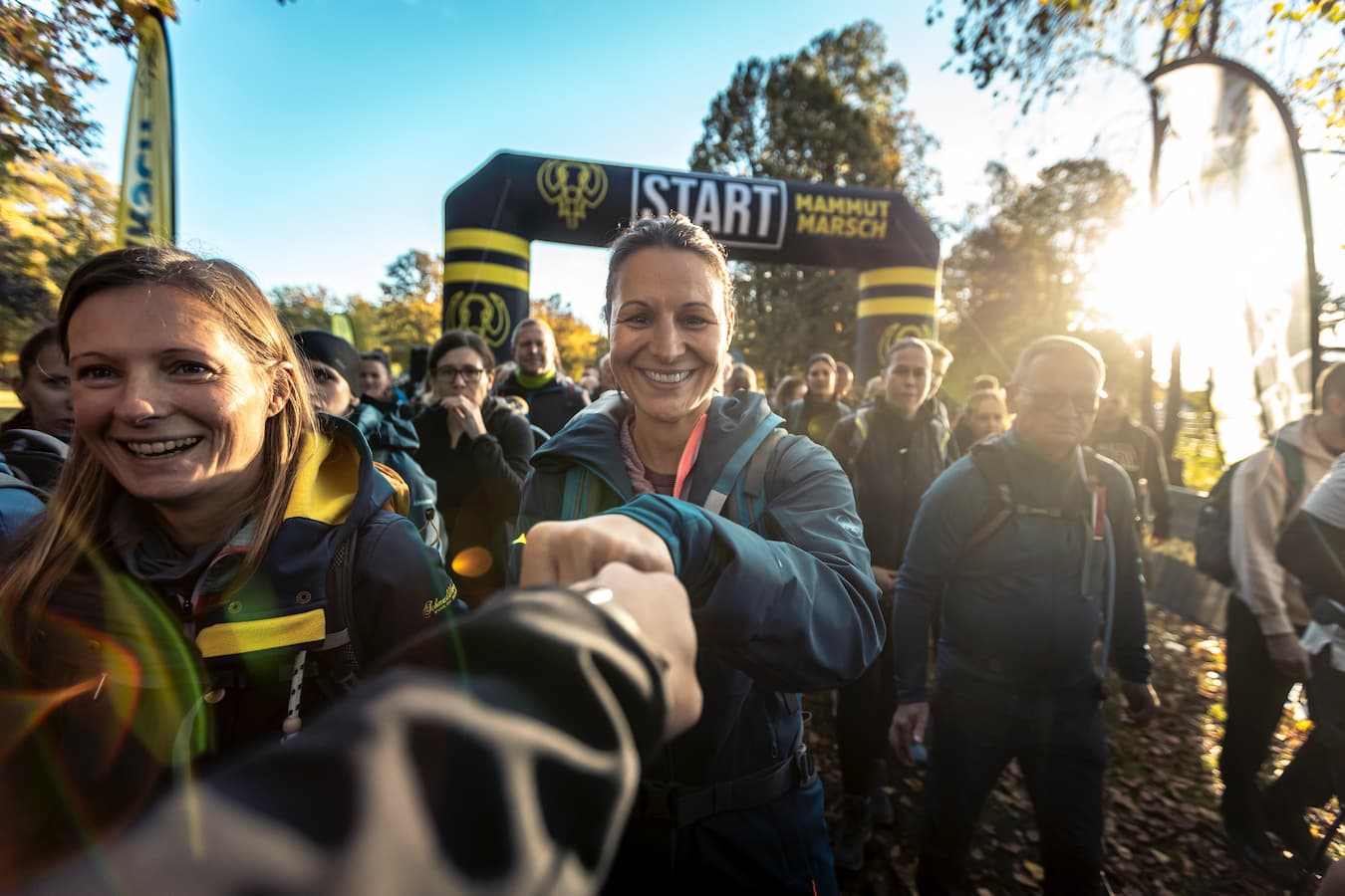 Teilnehmer des Mammutmarsch Stuttgart stehen motiviert am Startbogen und feiern den Beginn der Herausforderung bei Sonnenaufgang, bereit für die lange Wanderung. Motivierender Abklatsch.