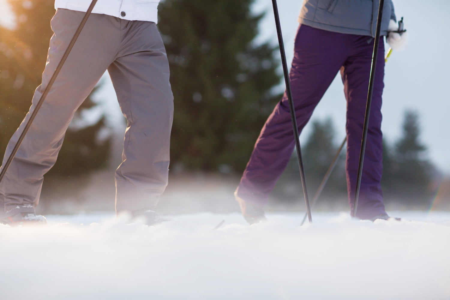 Beine von zwei Personen, die mit Wanderstöcken durch eine Winterlandschaft gehen