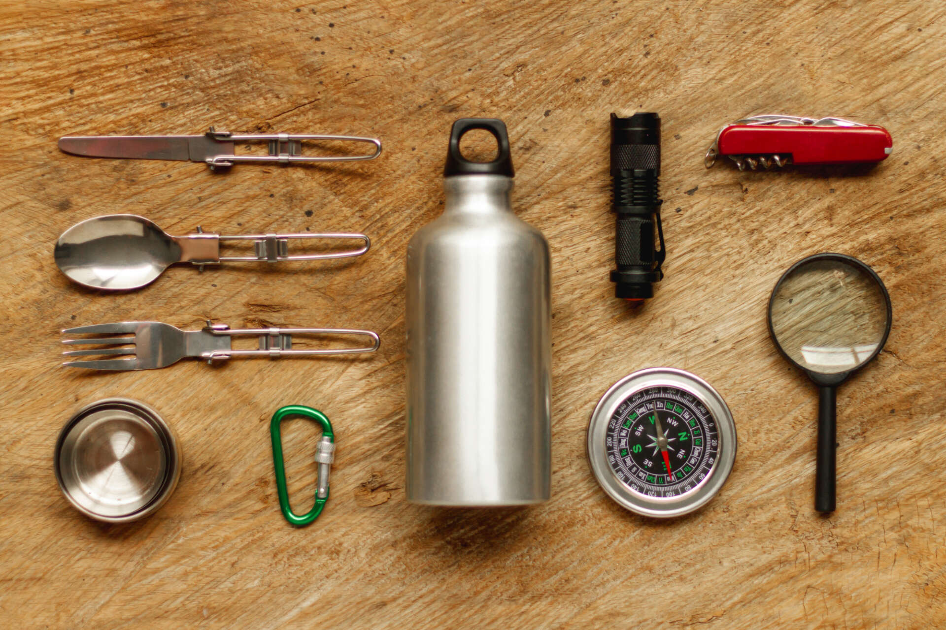 Das Bild zeigt ein Messer, einen Kompass, Besteck, eine Flasche und weiteres Zubehör zum Wandern.
