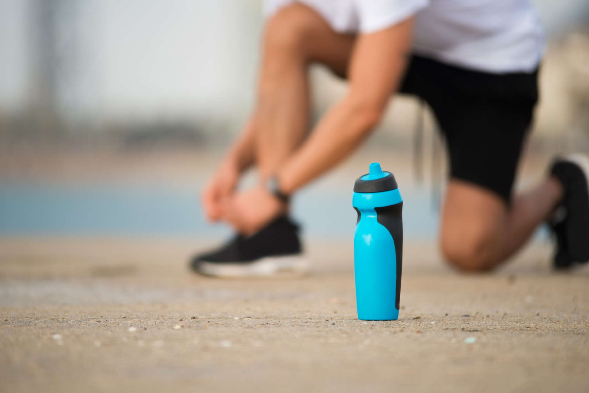 Eine Person bindet sich die Schuhe zu, vor ihr steht eine Sport-Trinkflasche.