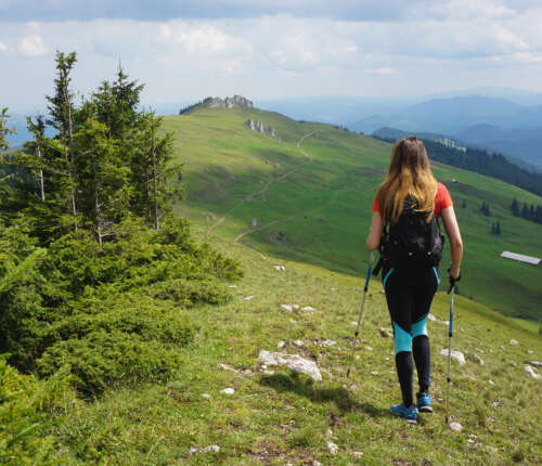 Wandern mit Stöcken: Eine Frau in Rückenansicht wandert über einen Bergkamm.