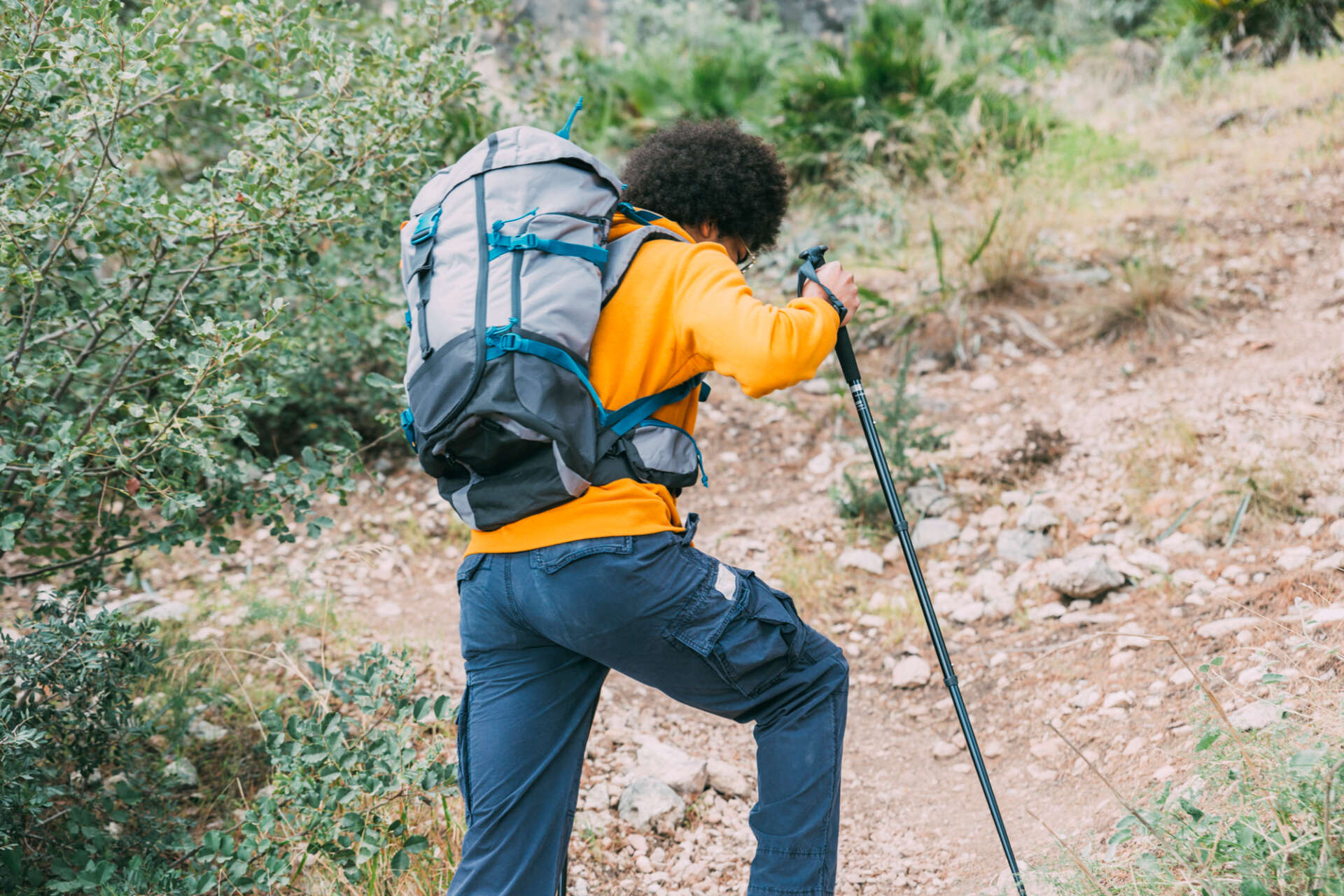 Ein Mann erklimmt beim Bergsteigen eine steile Anhöhe; dazu benutzt er Wanderstöcke.