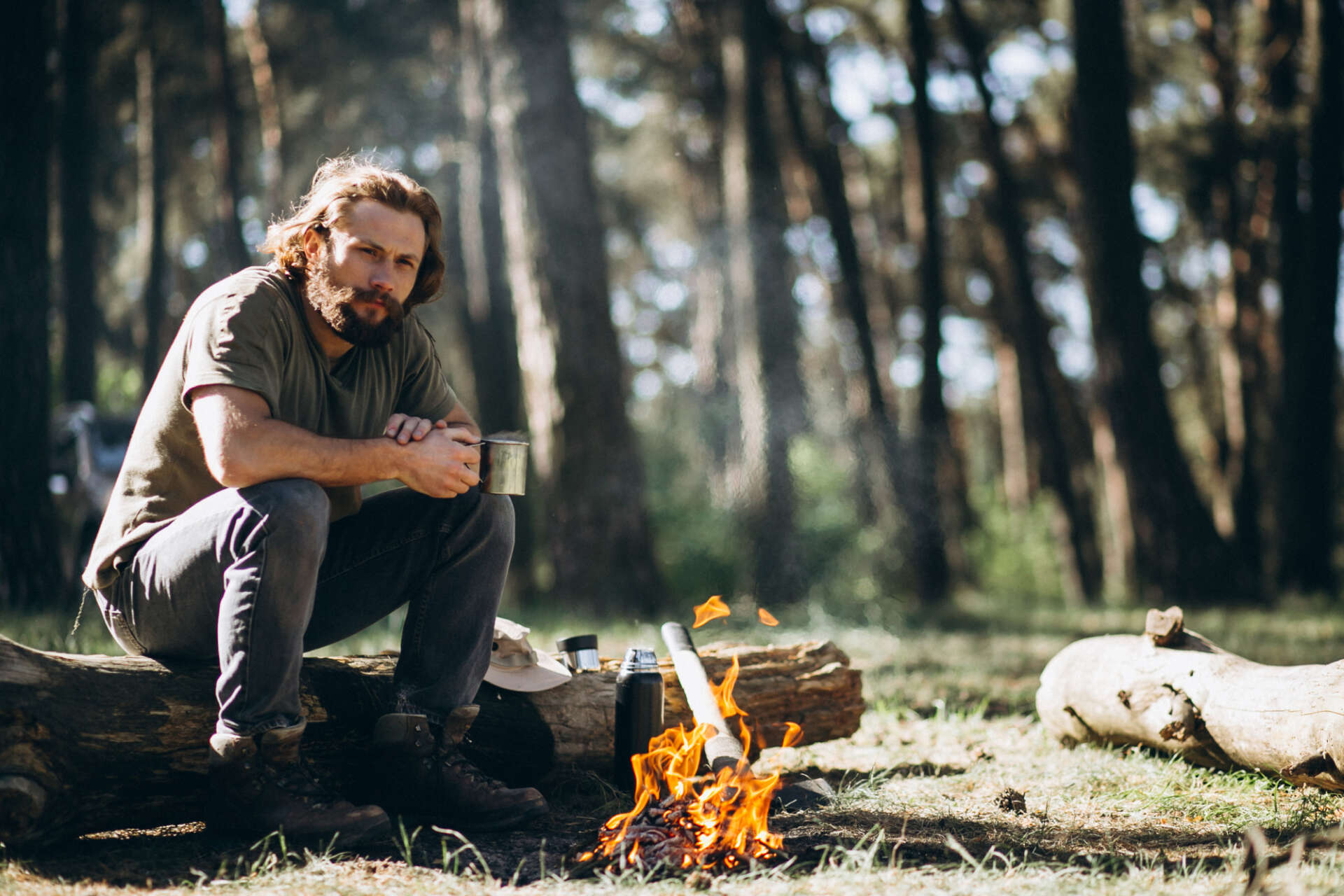 Ein Mann sitzt mit einer Tasse in der Natur am Feuer.