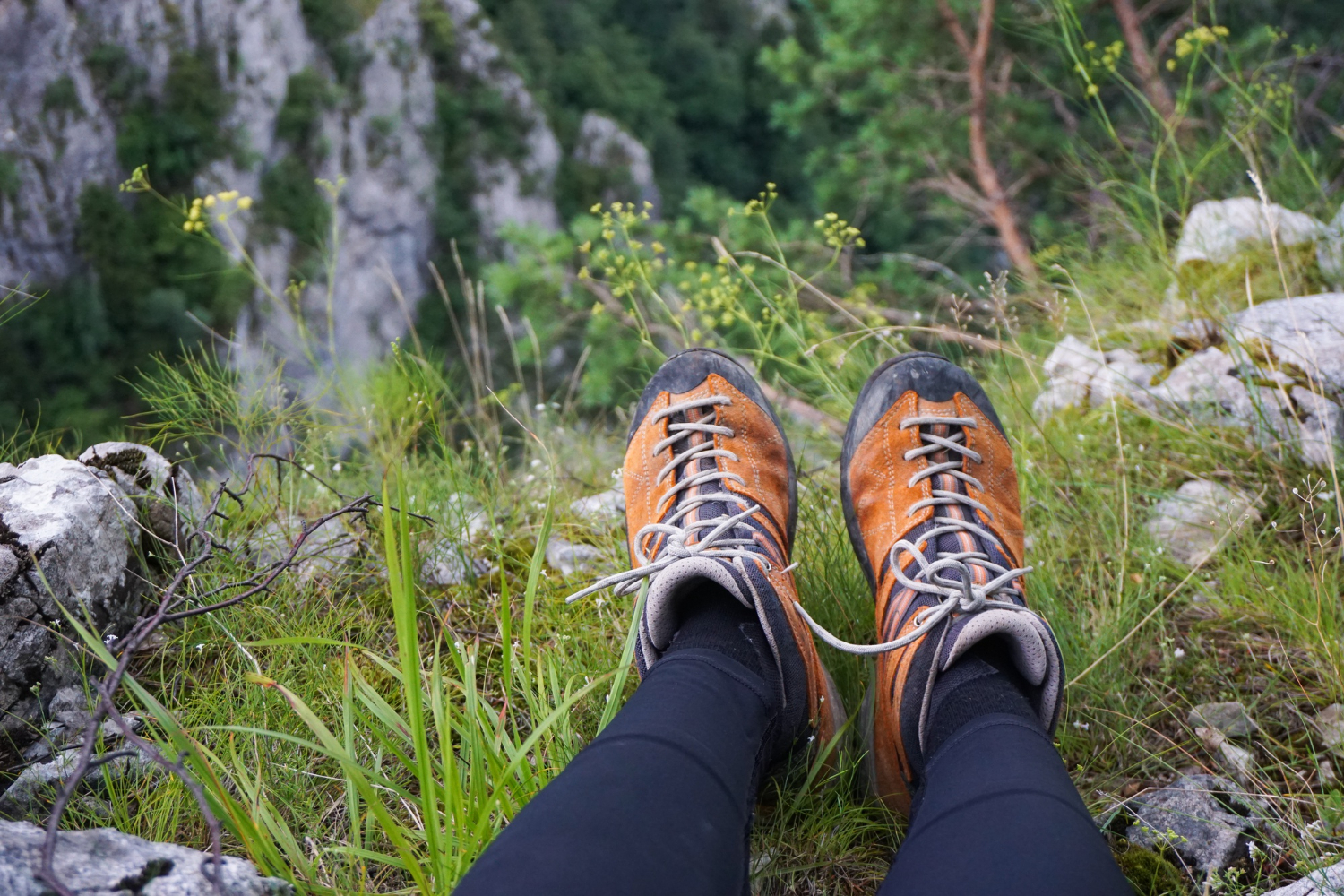 Eine Person sitzt auf einem Gipfel und genießt die Aussicht, zu sehen sind ihre Wanderschuhe. 