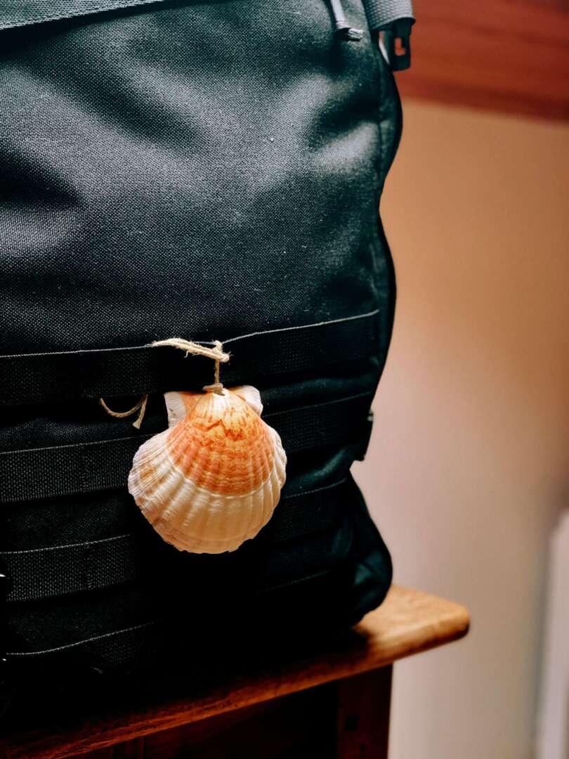 Ein Rucksack mit Anhänger in Form von Jakobsmuschel: Wie bekommt man in Deutschland den Pilgerausweis?