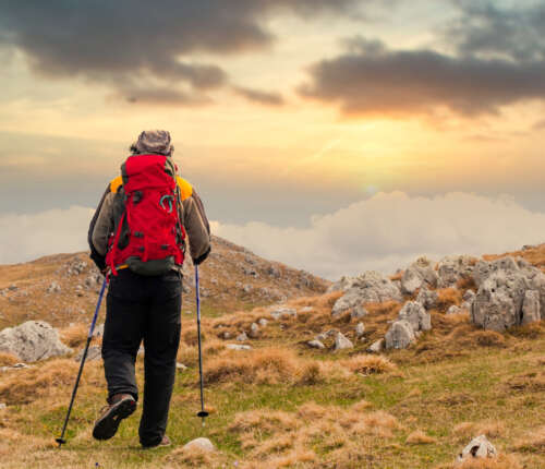 Ein Wanderer wandert mit Wanderstöcken dem Sonnenuntergang entgegen.