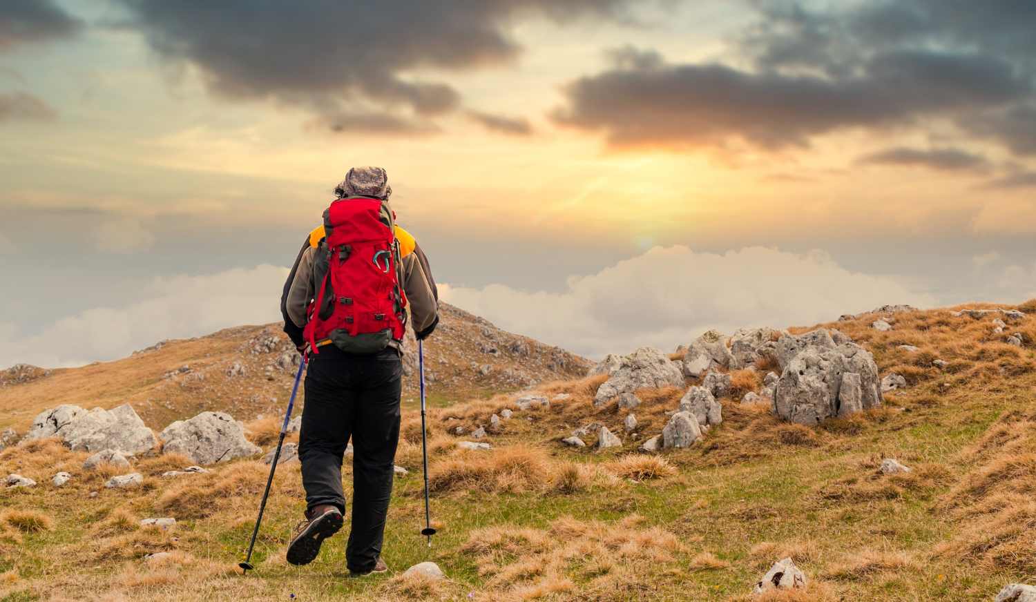 Ein Wanderer wandert mit Wanderstöcken dem Sonnenuntergang entgegen.