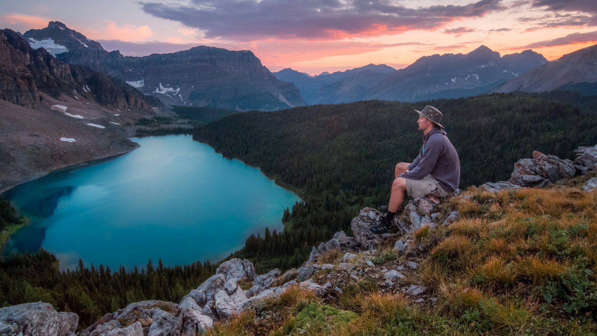 Mehrtägiger Wanderurlaub: Ein Mann in den Bergen blickt auf einen wunderschönen Bergsee. Wichtig: Eine spezielle Packliste. 