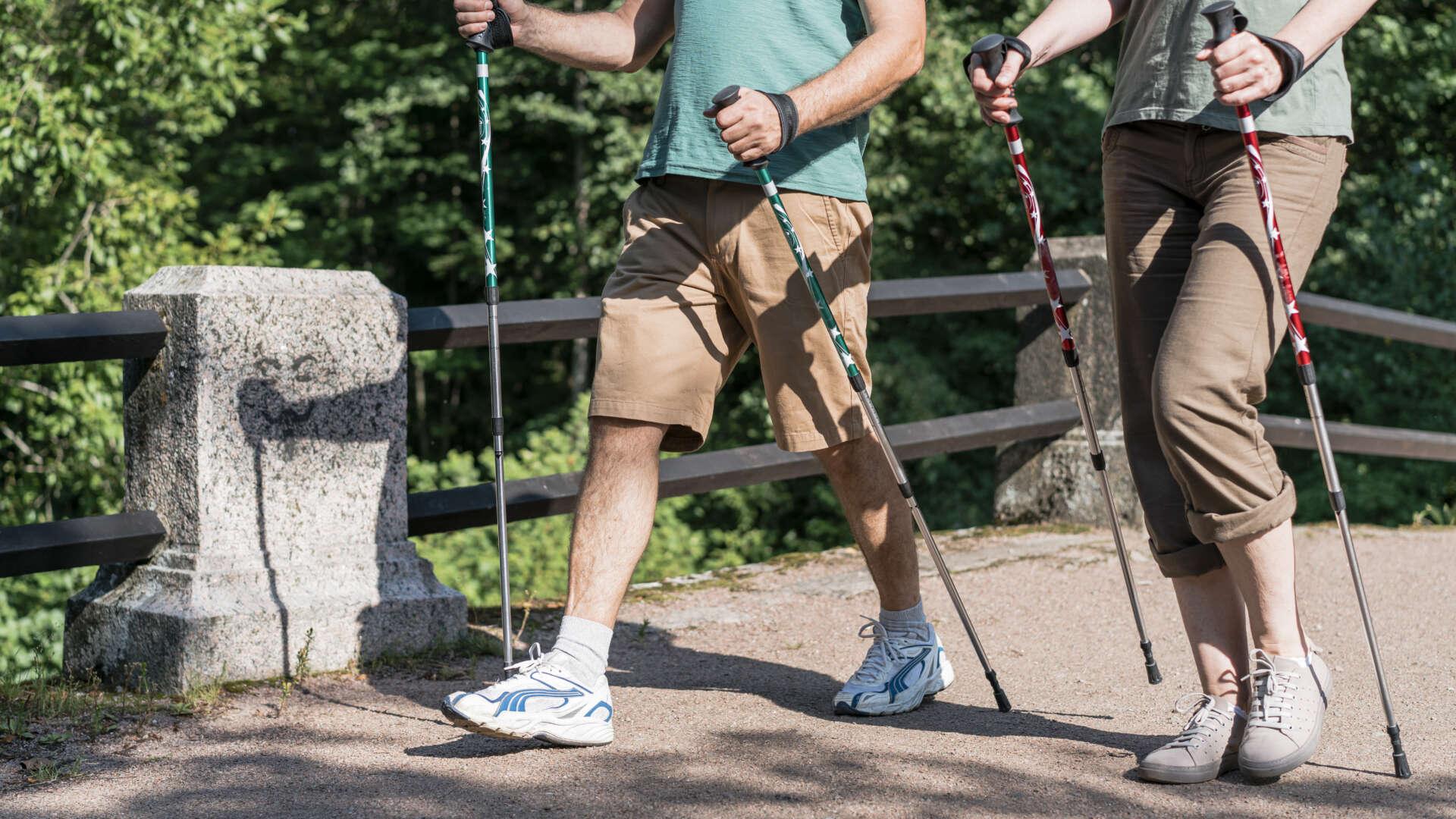 Zwei Personen beim Nordic Walking auf einem Waldweg mit unterschiedlichen Schuhmodellen