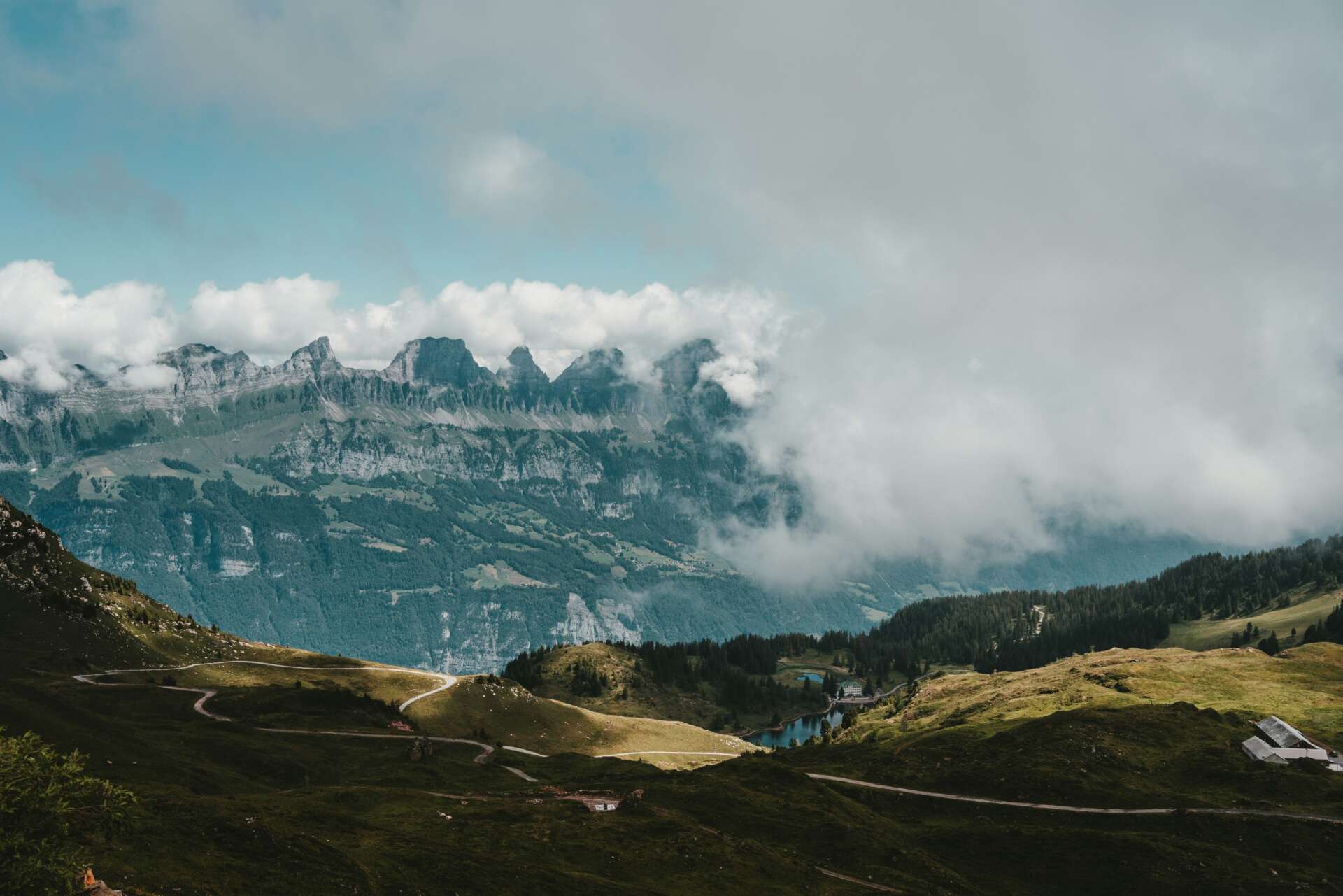 Blick auf die Churfirsten mit grünen Almen, Wanderwegen und tief hängenden Wolken oberhalb des Walensees.